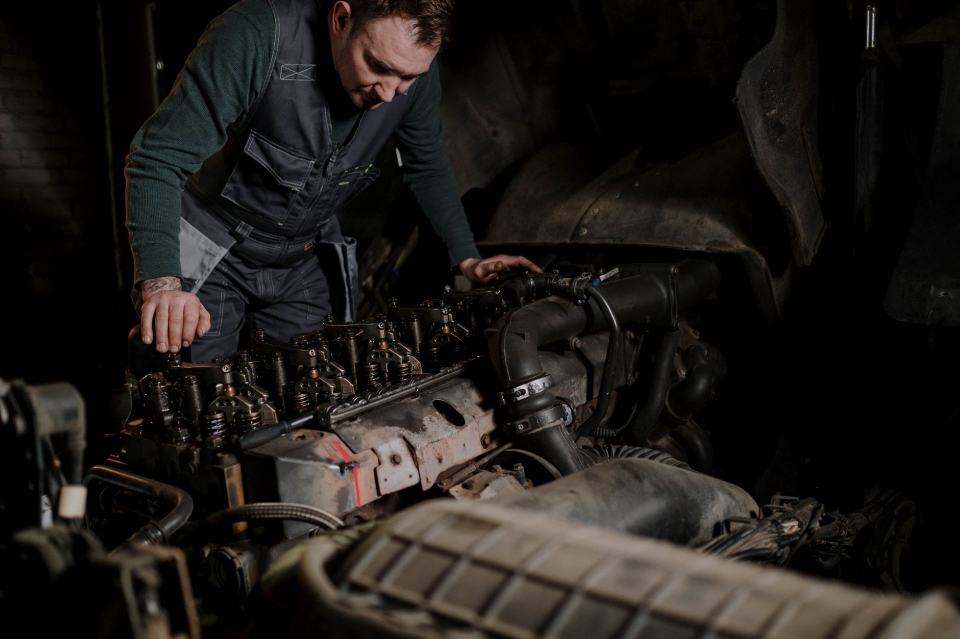 A mechanic working on an engine in a dark workshop